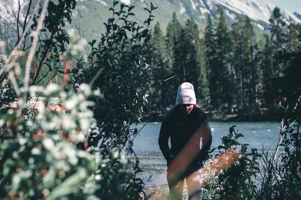 person in black shirt and white cap sitting on brown rock near body of water during