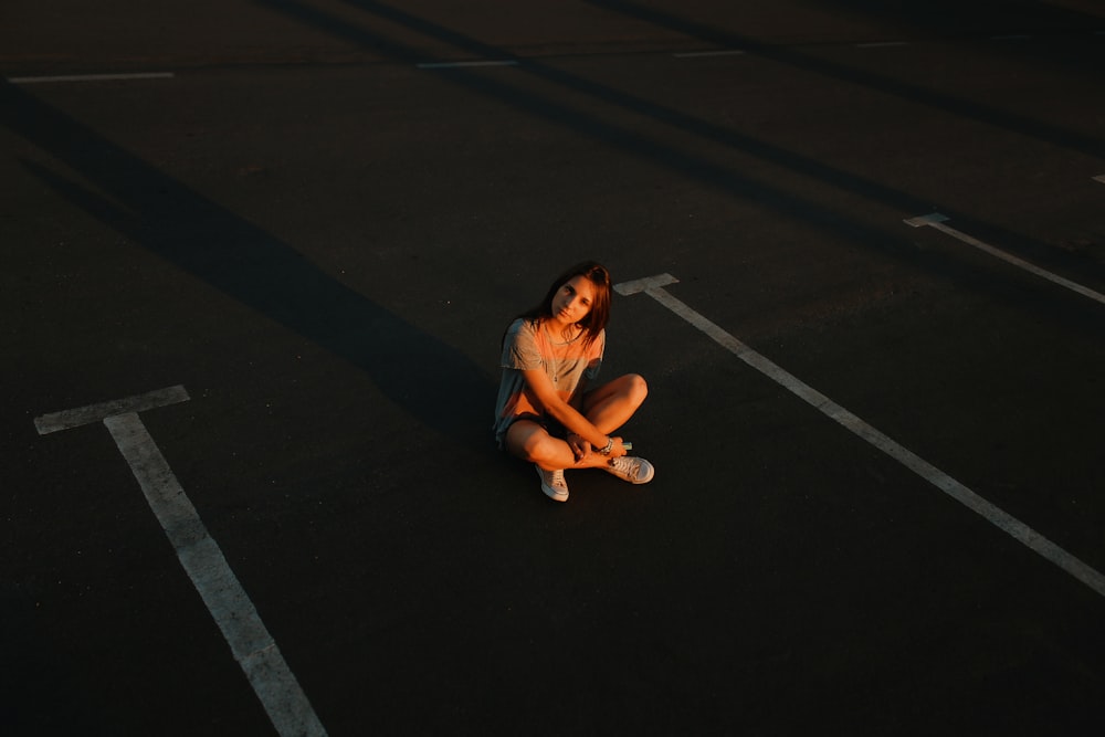 woman in gray tank top and blue denim shorts sitting on black asphalt road during daytime