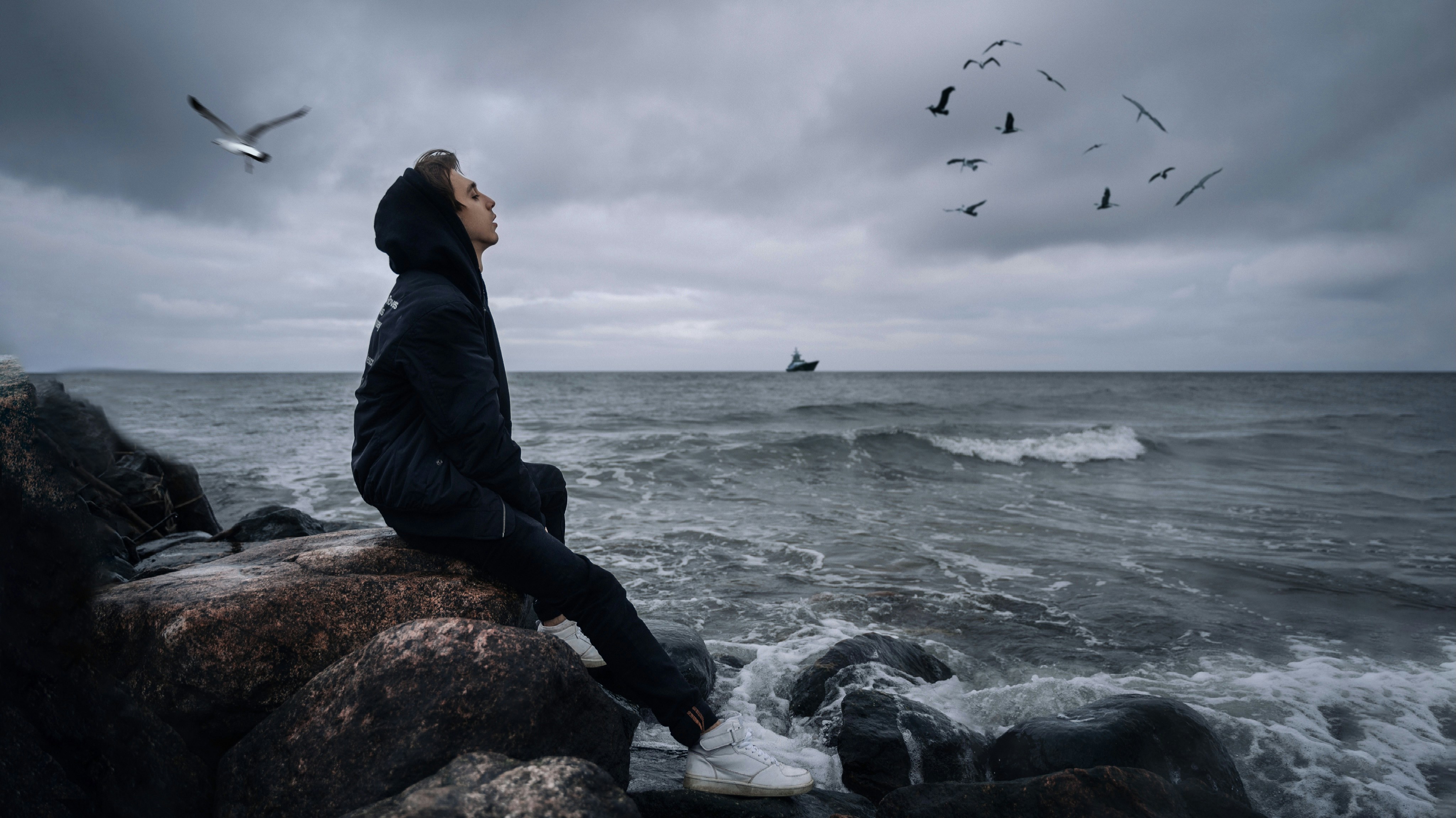 man in black jacket sitting on rock near sea during daytime