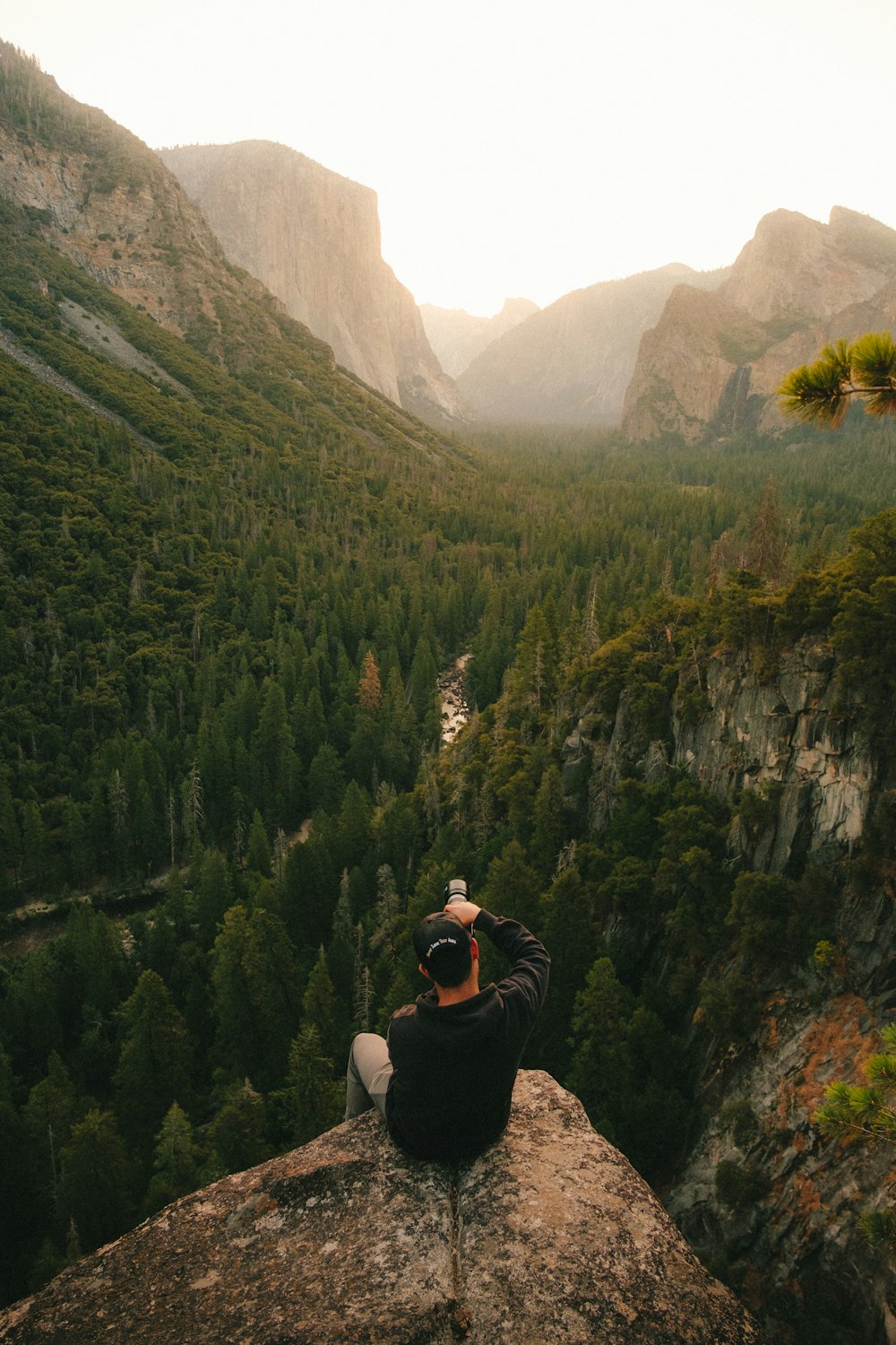 黒いジャケットと黒いズボンを着た男が岩の上に座り、昼間、緑の山々を眺めている
