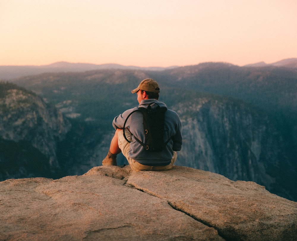 man in black t-shirt and brown hat sitting on rock