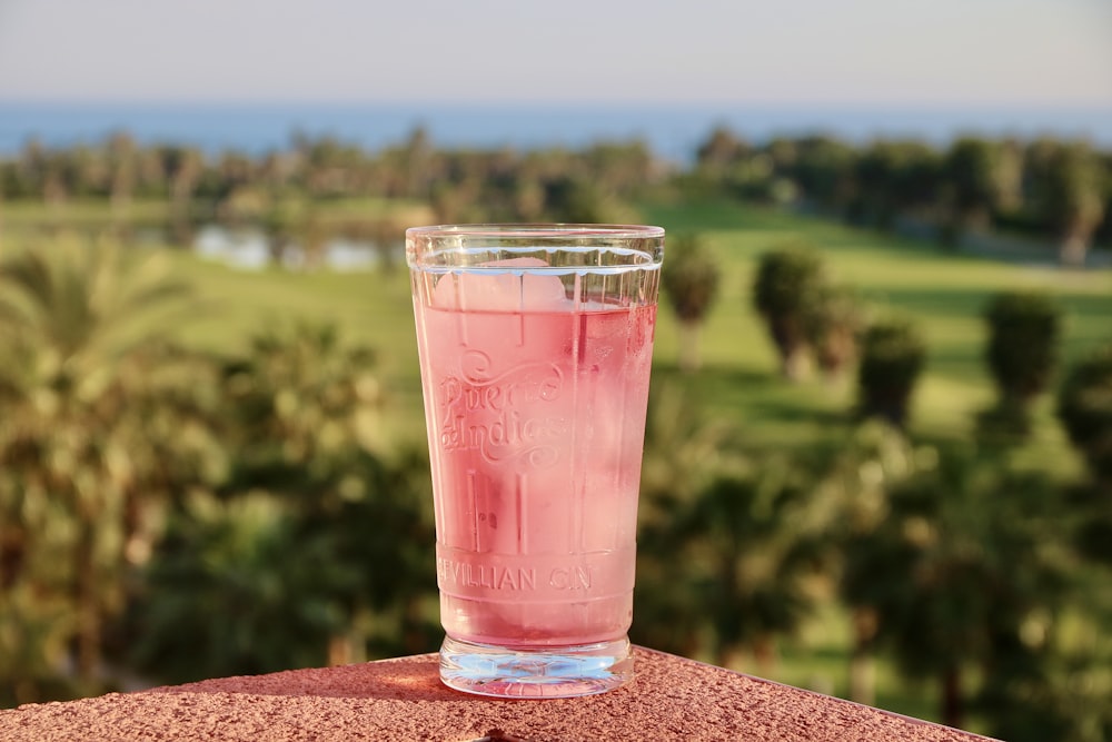 clear drinking glass with red liquid on brown concrete surface