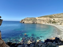 brown rocky mountain beside blue sea under blue sky during daytime