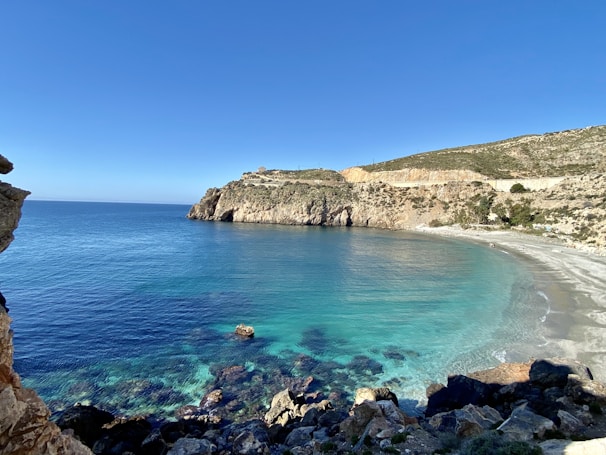 brown rocky mountain beside blue sea under blue sky during daytime