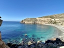 brown rocky mountain beside blue sea under blue sky during daytime