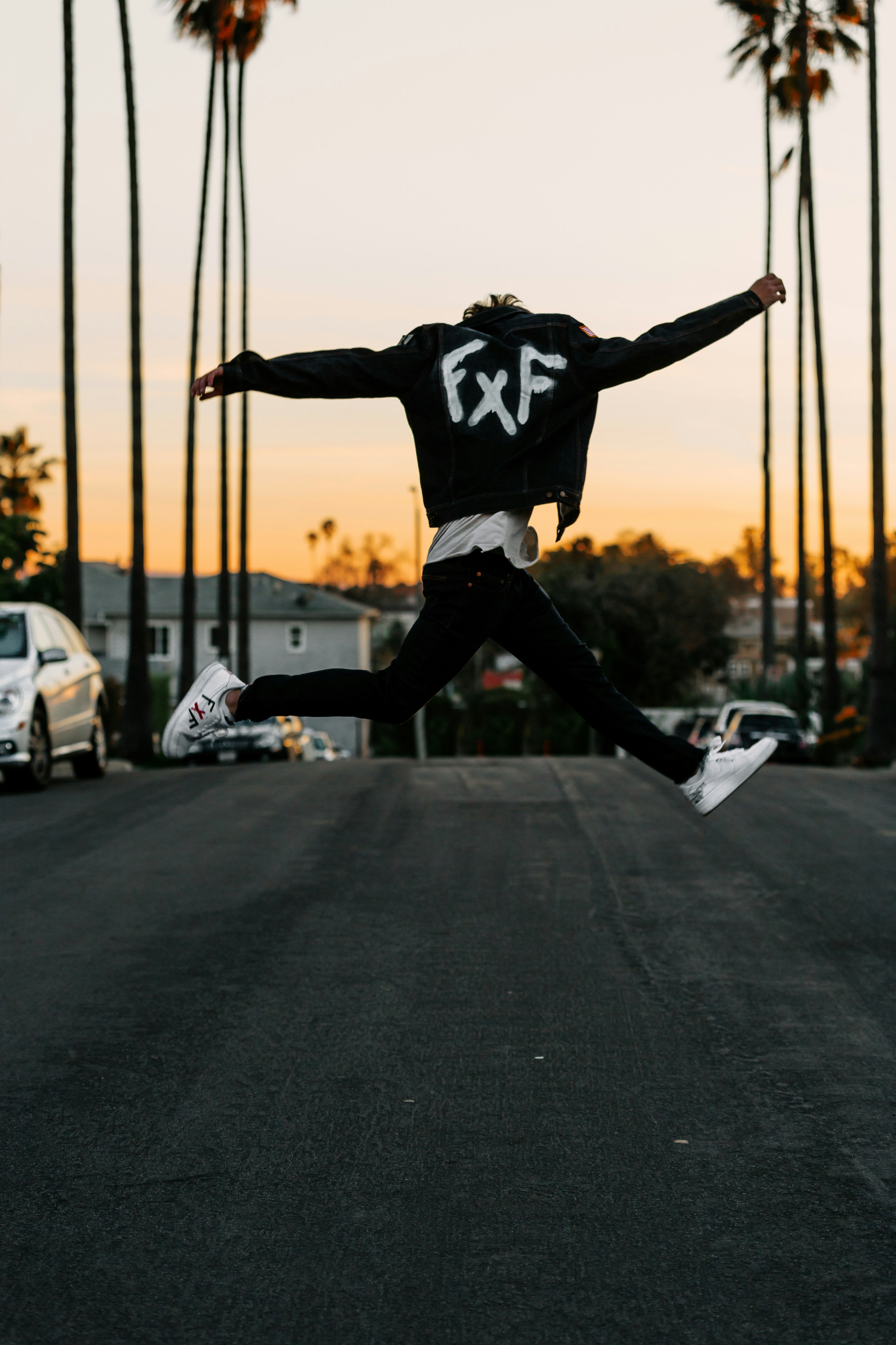 Mann in schwarz-weißer Jacke und schwarzer Hose springt tagsüber auf schwarze Asphaltstraße
