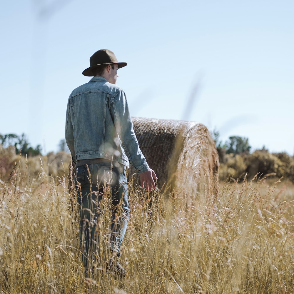 homem em camisa de manga comprida cinza e chapéu marrom em pé no campo de grama marrom durante o dia