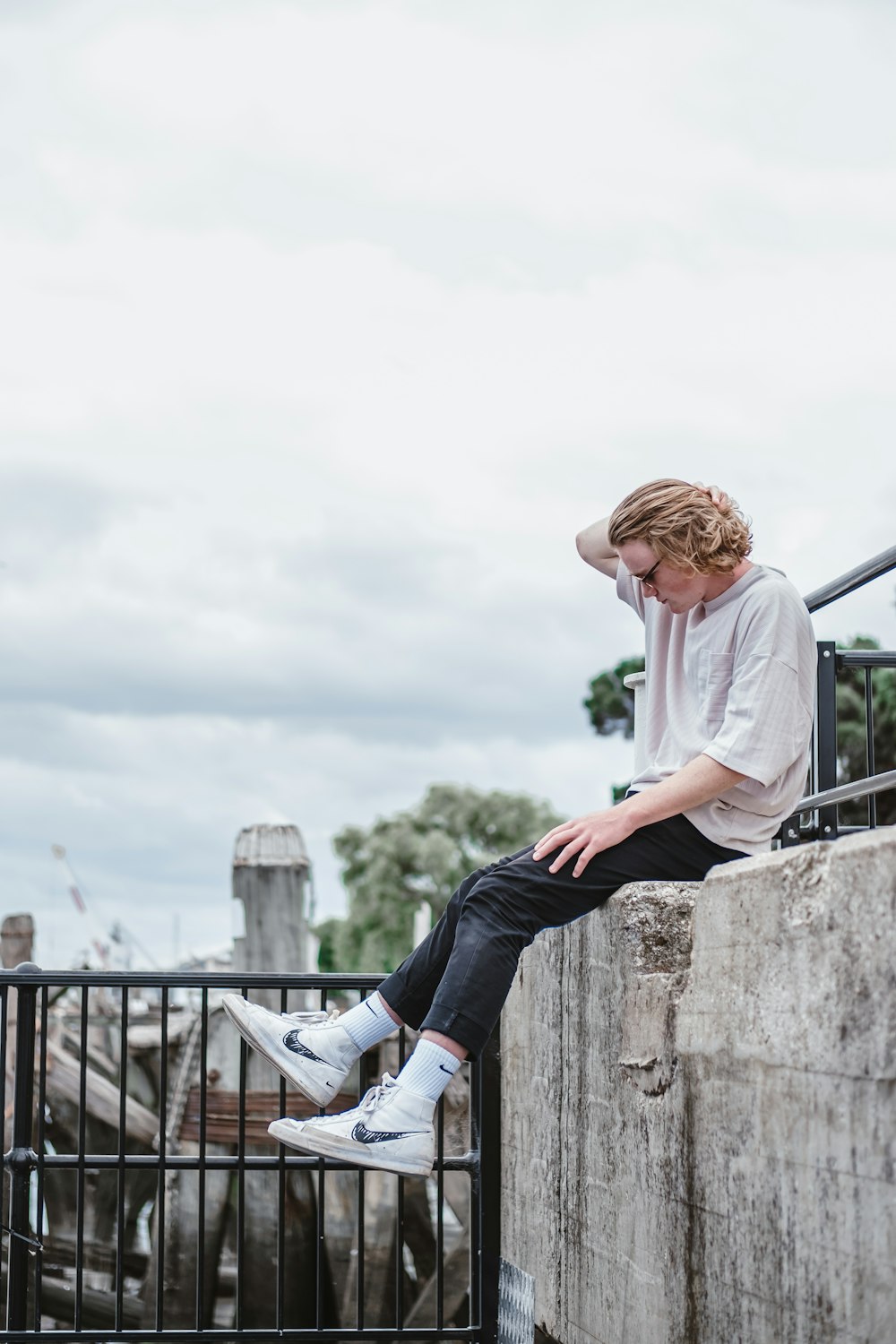 woman in white long sleeve shirt and blue denim jeans sitting on gray concrete fence during