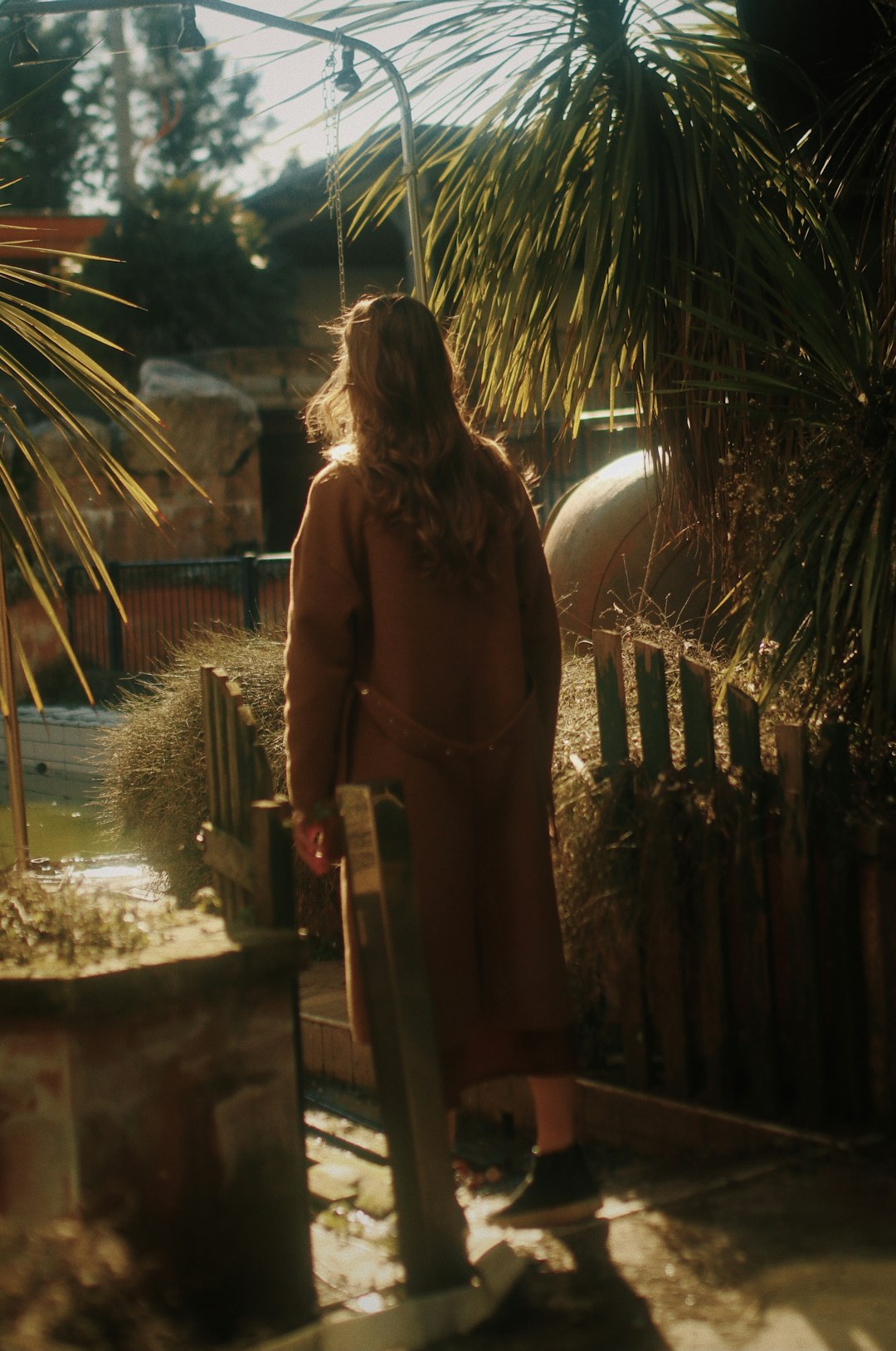 woman in brown long sleeve dress standing near brown wooden fence during daytime