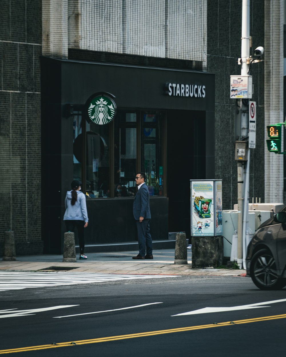 昼間、黒と白の店の近くに立つ黒いジャケットと青いデニムジーンズの男