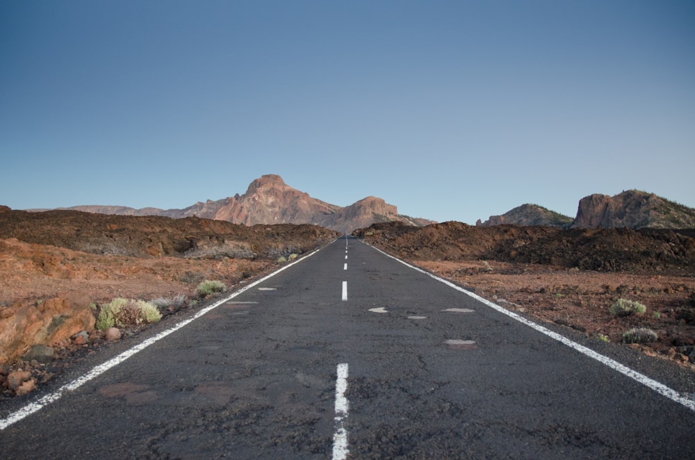 gray concrete road near brown mountain under blue sky during daytime