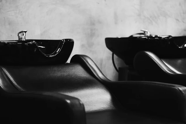 Black and white photo of a sleek salon interior with gold accents highlighting the styling stations.