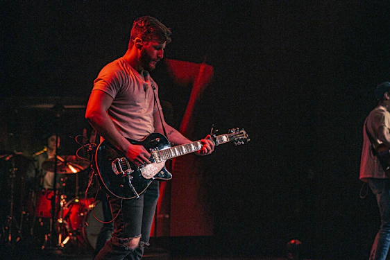 Dominic Holmes passionately playing guitar on stage with warm lighting and an engaged audience.