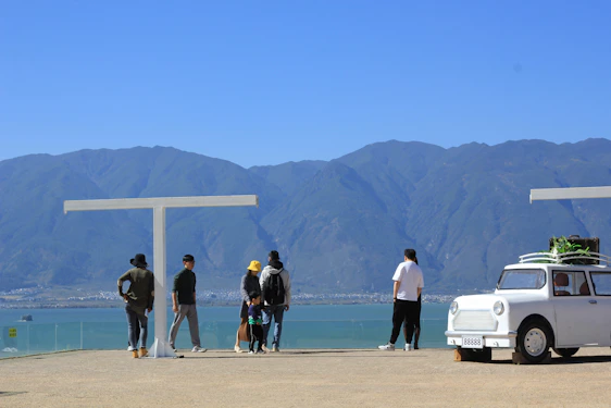 A vibrant scene of happy tourists boarding a comfortable rental car with scenic mountains in the background.