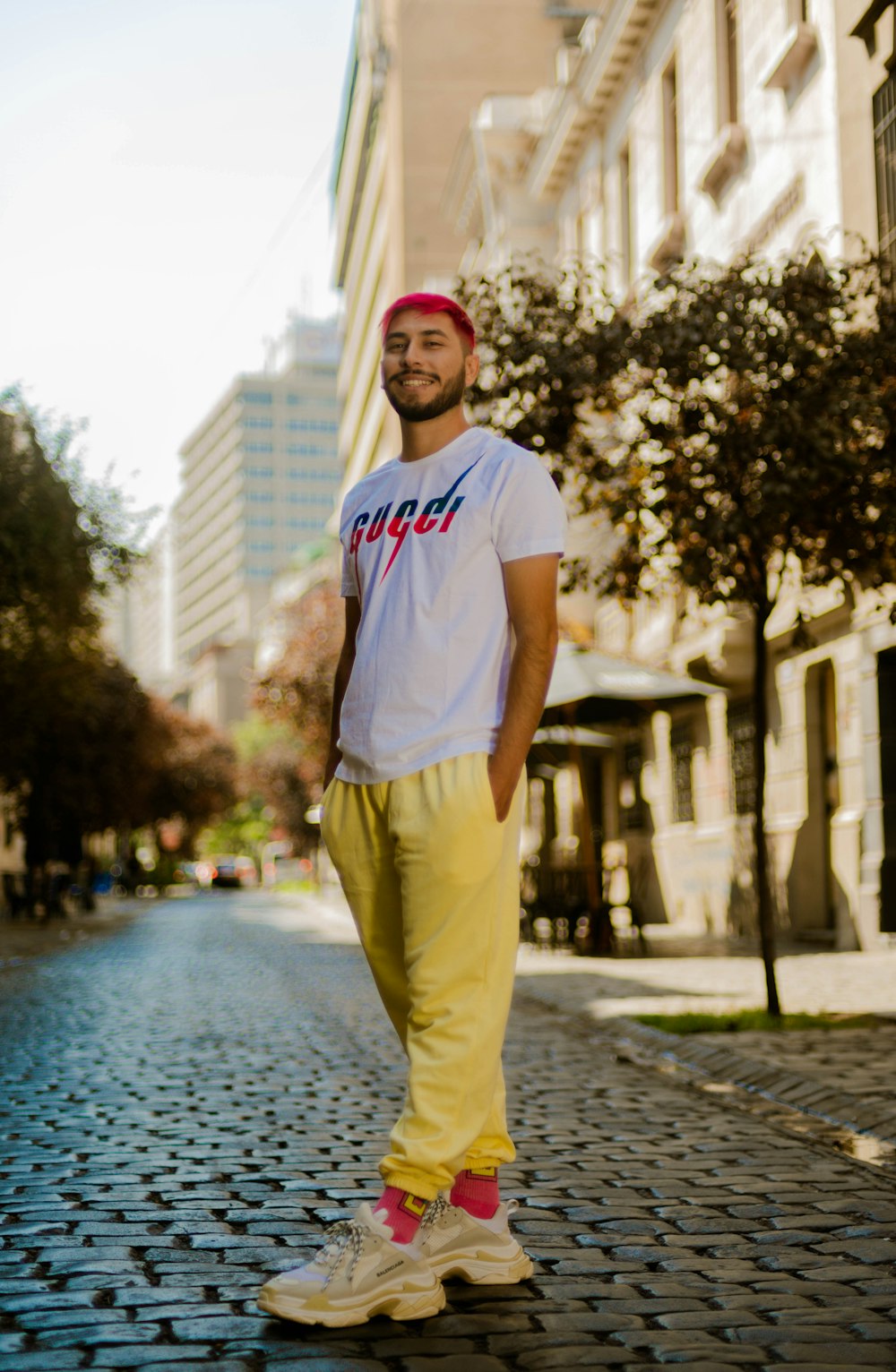 man in white crew neck t-shirt and yellow pants standing on gray concrete pavement during