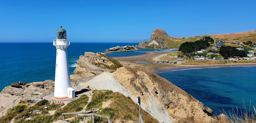 white lighthouse on brown rocky hill near body of water during daytime