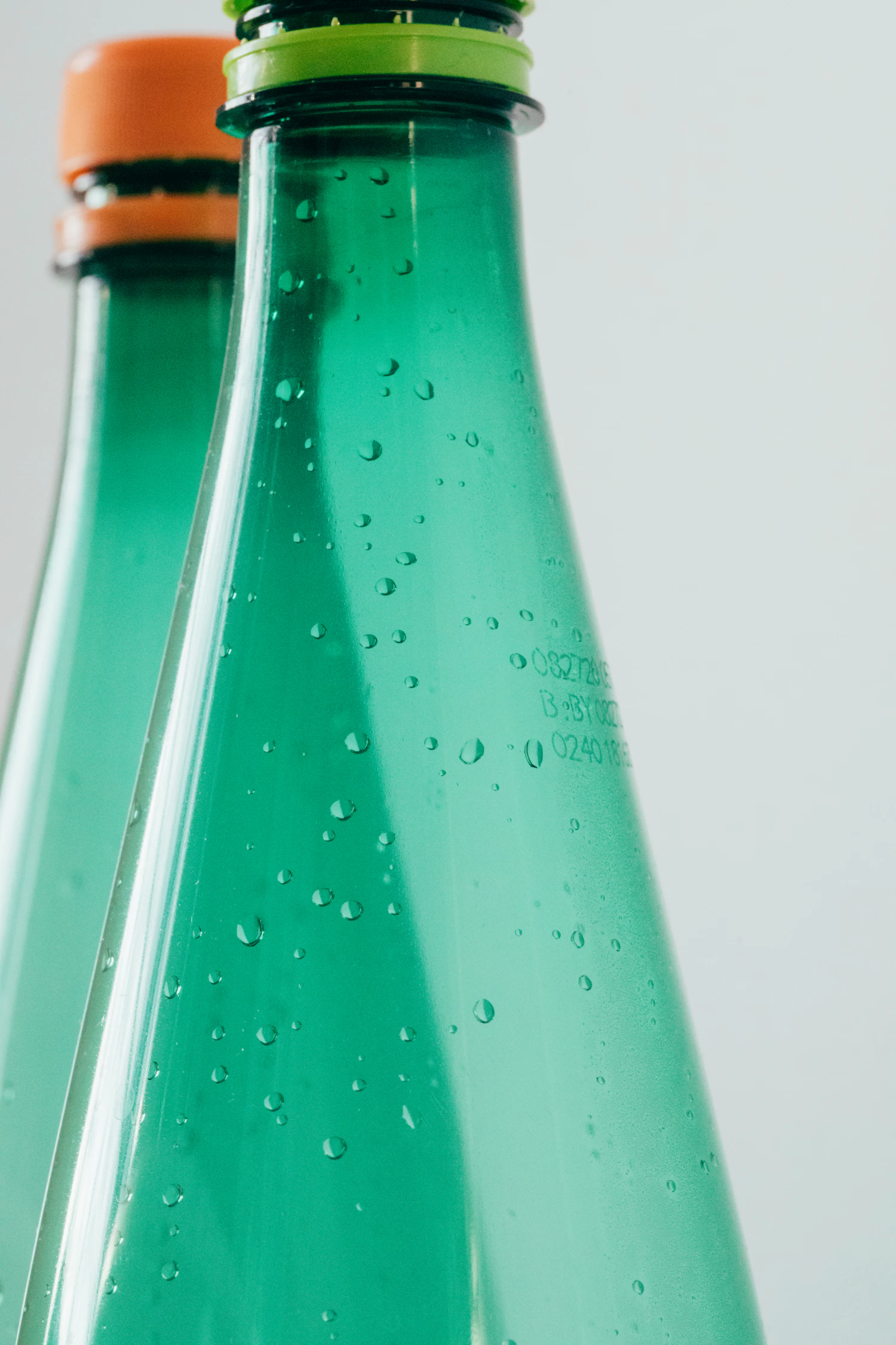 Two green glass soda bottles beaded with condensation, shoulder to shoulder
