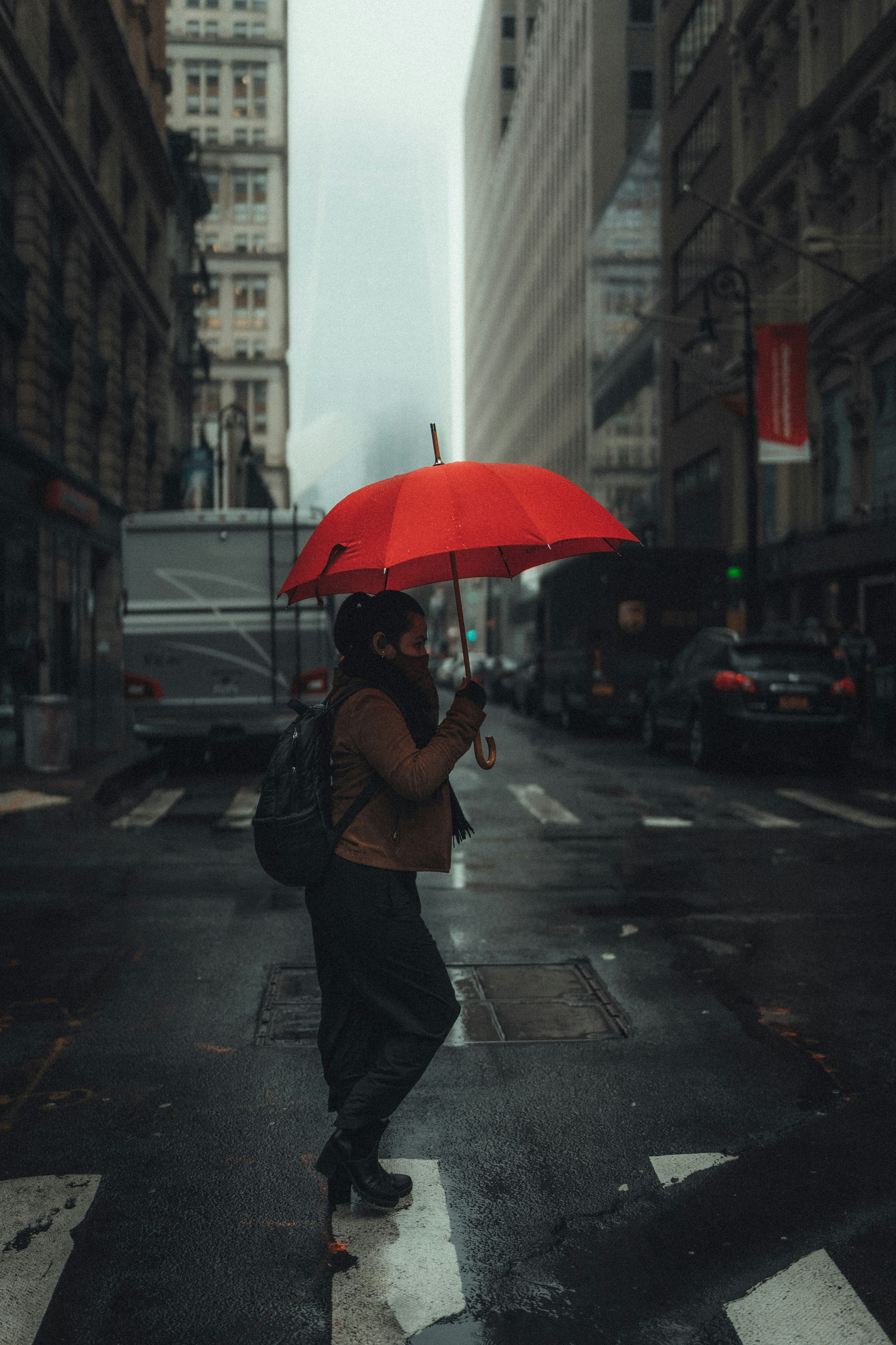 man in black jacket holding umbrella while walking on pedestrian lane during daytime