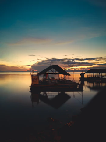 A sleek modern floating house on calm water at sunset, reflecting warm light.