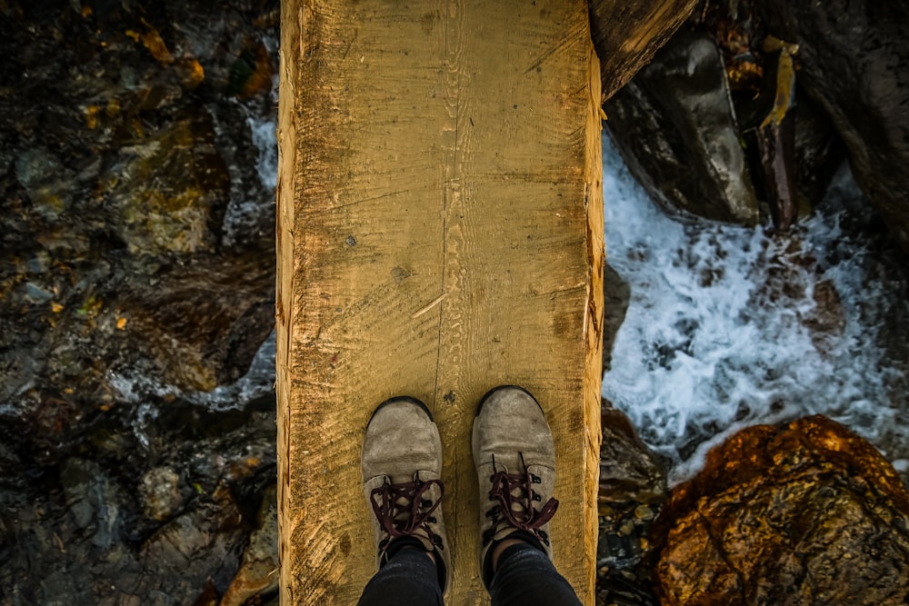 person in black pants and brown shoes standing on brown wooden plank