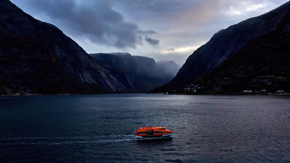 Orangefarbenes Boot tagsüber auf dem Wasser in der Nähe des Berges