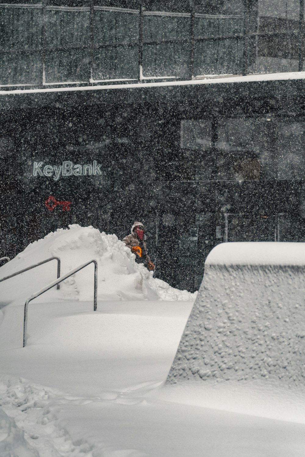 Hombre en chaqueta roja sentado en banco cubierto de nieve blanca durante el día