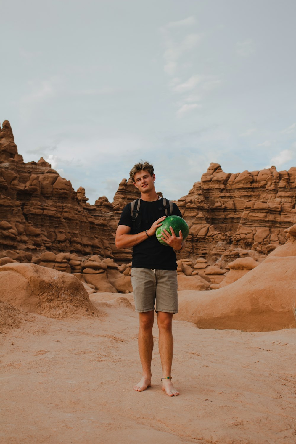 man in black t-shirt and blue denim shorts standing on brown rock formation during daytime