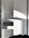 A white cabinet with multiple compartments, including a partially open drawer. Soft natural light creates shadows and highlights on the surface. A person is partially visible at the bottom right corner, possibly assembling or inspecting the cabinet.