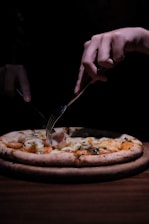 person holding stainless steel fork and knife slicing pizza