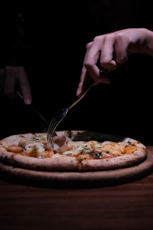 person holding stainless steel fork and knife slicing pizza