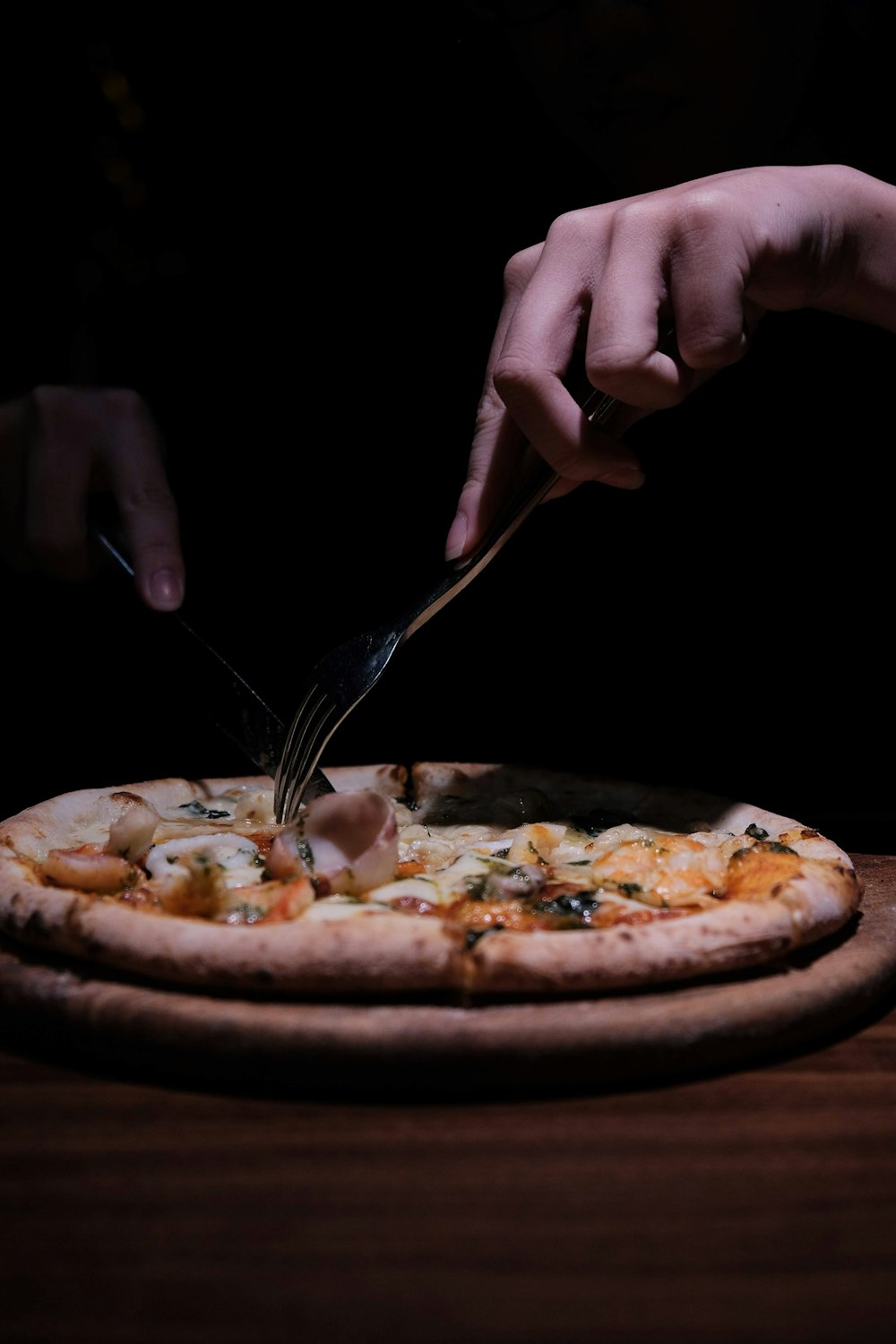 Person mit Edelstahlgabel und Messer schneiden Pizza