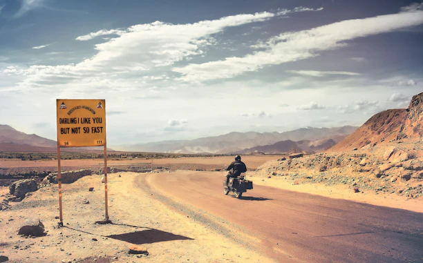 man in black motorcycle on brown sand under white clouds and blue sky during daytime