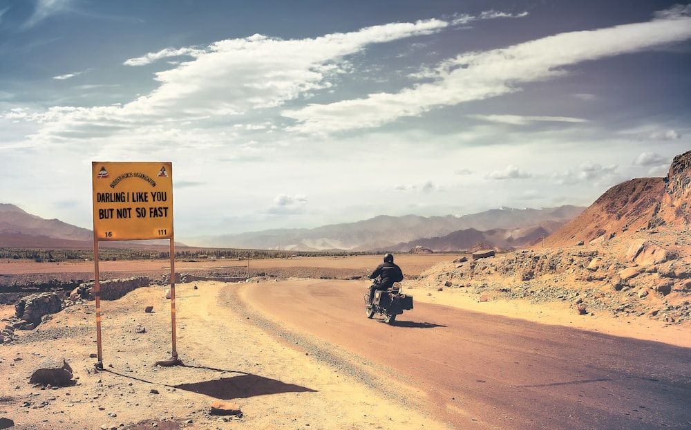 Mann in schwarzem Motorrad auf braunem Sand unter weißen Wolken und blauem Himmel tagsüber