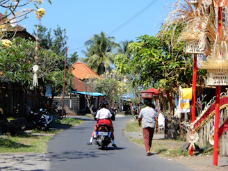 A friendly local driver on a scooter smiling warmly with a scenic Bali village in the background.