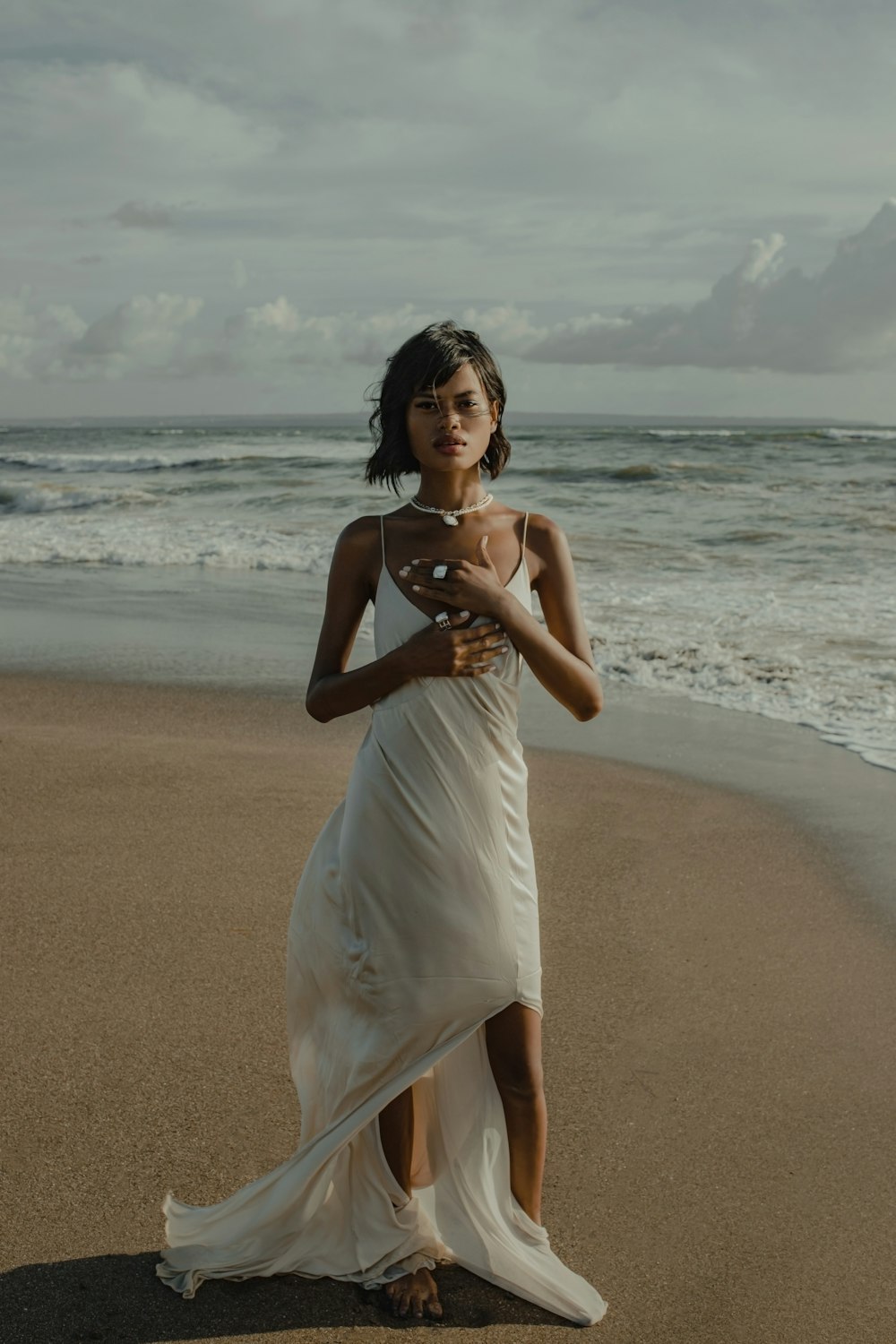 Mujer con vestido blanco de pie en la playa durante el día