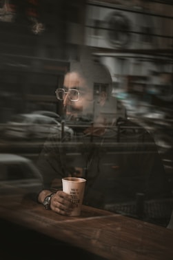 man in black leather jacket holding brown disposable cup