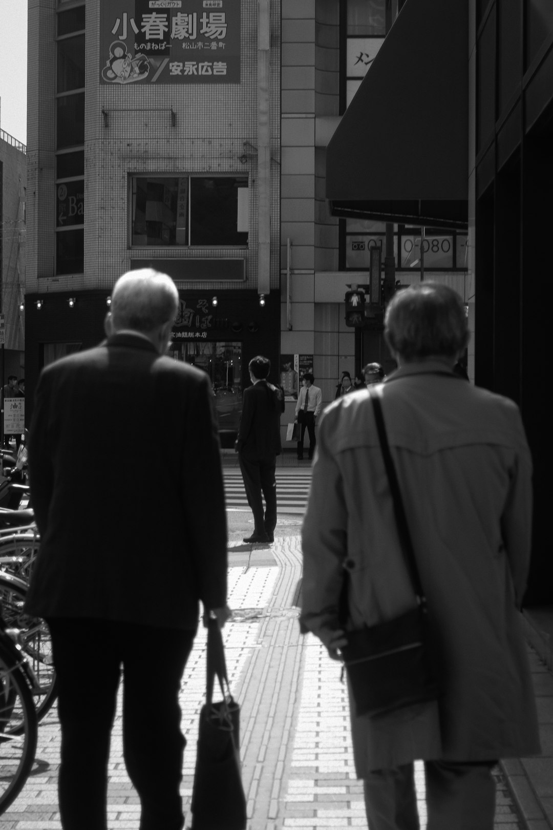 grayscale photo of man in suit jacket walking on sidewalk