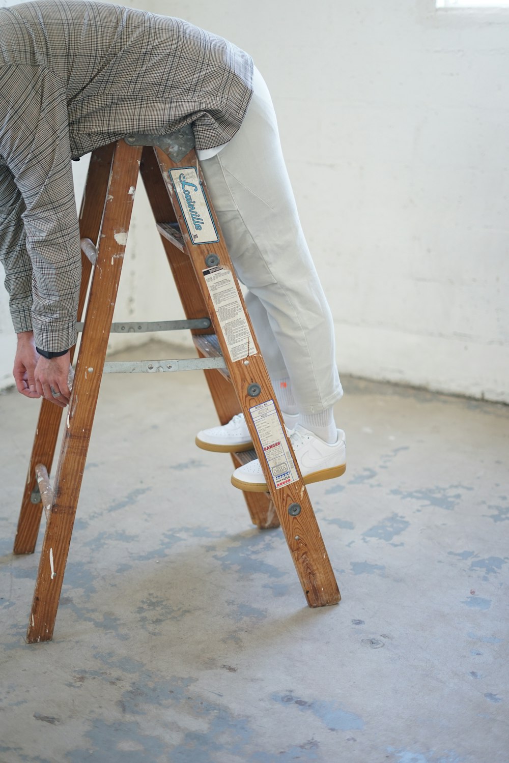 Persona in camicia a quadri grigia e bianca e jeans blu in denim che tiene skateboard di legno marrone