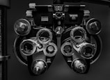 A close-up view of an optometry device called a phoropter, used for testing individual lenses on each eye during an eye exam. The device is composed of multiple dials, lenses, and knobs.
