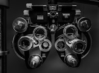 A close-up view of an optometry device called a phoropter, used for testing individual lenses on each eye during an eye exam. The device is composed of multiple dials, lenses, and knobs.