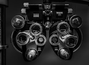 A close-up view of an optometry device called a phoropter, used for testing individual lenses on each eye during an eye exam. The device is composed of multiple dials, lenses, and knobs.