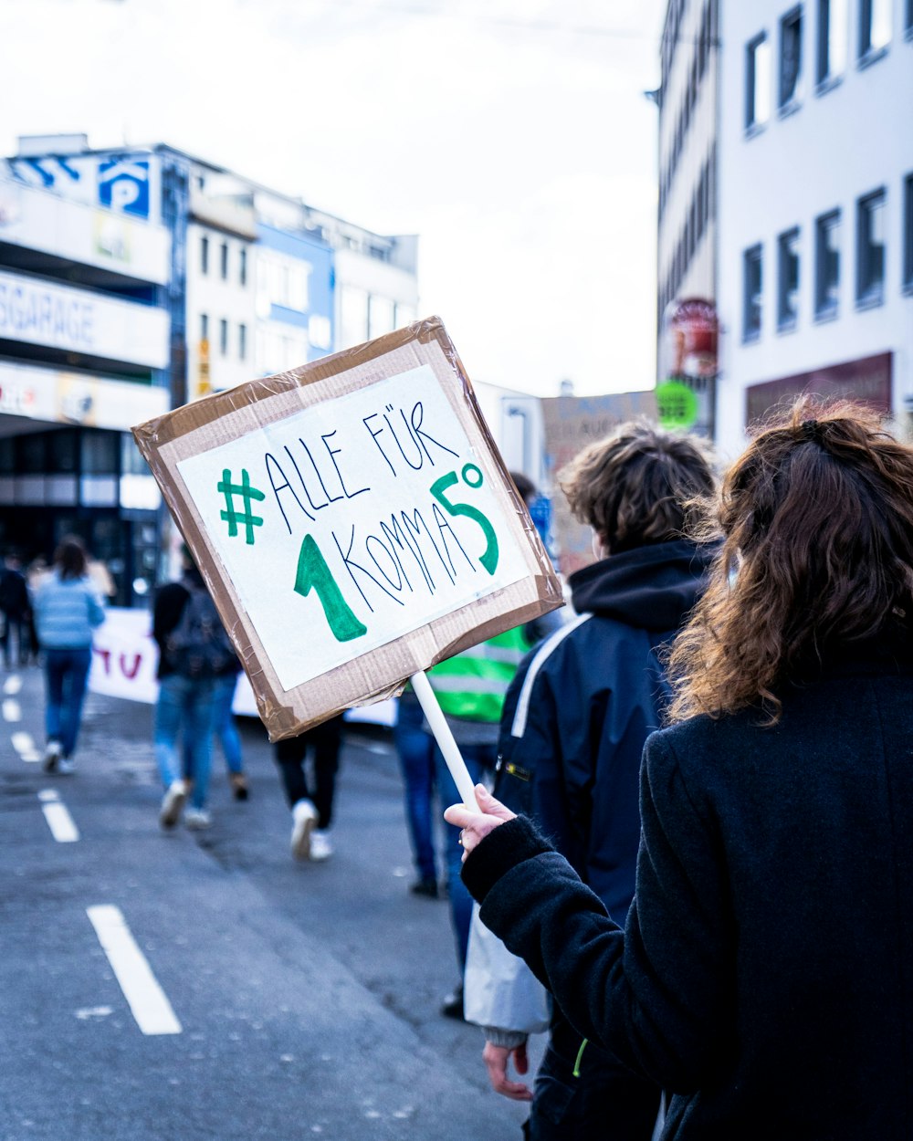 woman in blue jacket holding brown and green sign