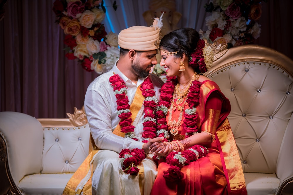 woman in red and gold sari sitting beside woman in white dress