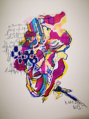 An abstract and colorful artwork with various vibrant hues, including red, blue, yellow, and pink. It appears to include abstract shapes and lines with a possible figure or face partially visible among the colors. Handwritten text and doodles are blended into the design, creating a layered and textured appearance.
