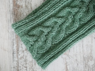 A close-up of a soft, chunky knit sweater draped over a wooden chair by a frosted window.