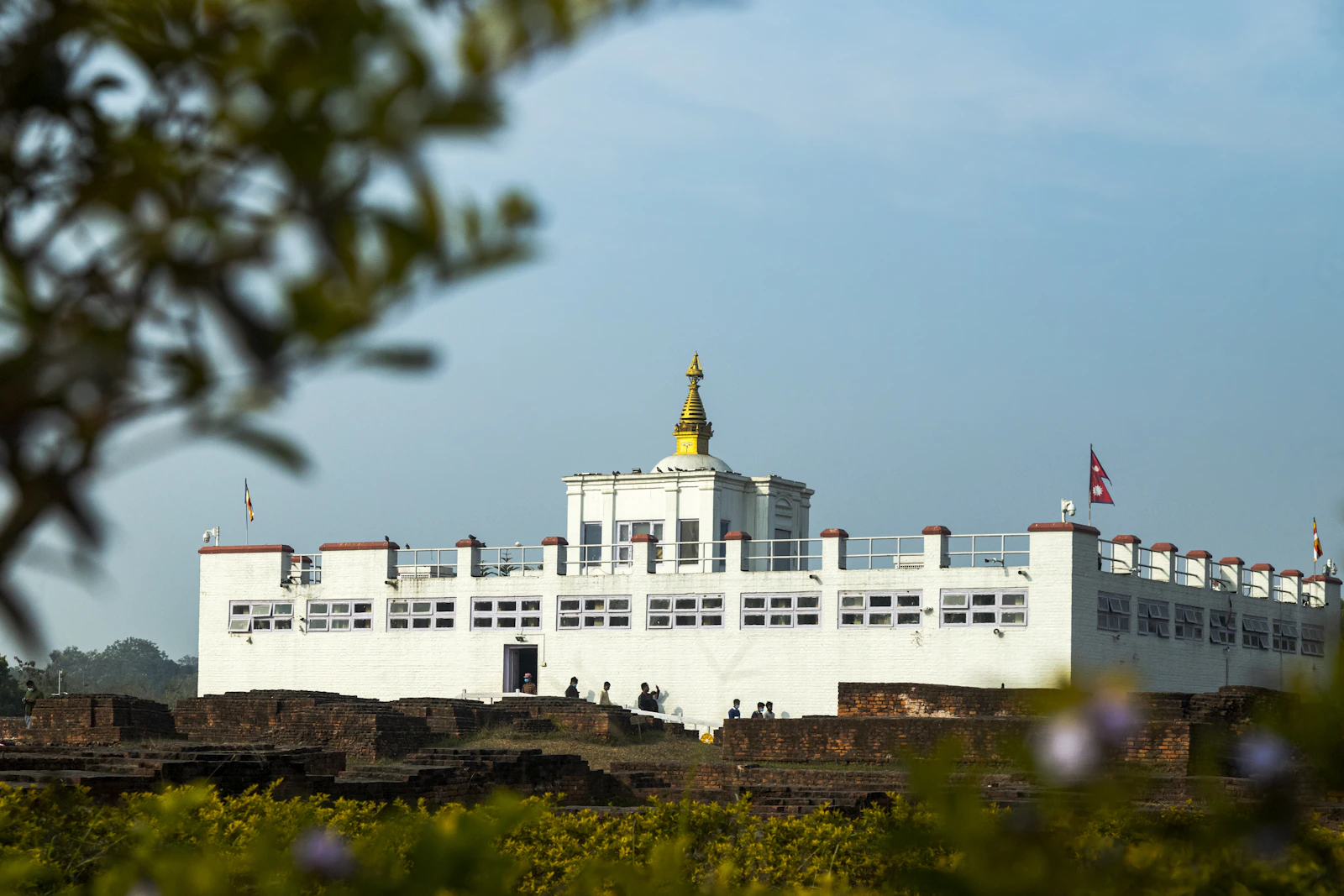 The white Maya Devi Temple at Lumbini above the excavated brick foundations of older shrines, a Nepali flag beside it