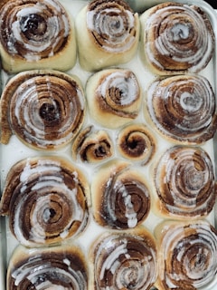 A tray of freshly baked cinnamon rolls with swirls of icing dripping gently