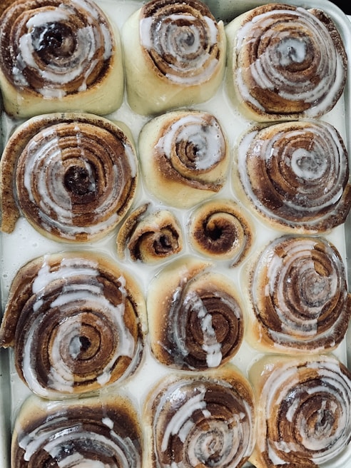 A tray of freshly baked cinnamon rolls with swirls of icing dripping gently