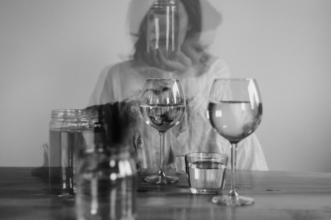 grayscale photo of woman in long sleeve shirt sitting beside table with wine glass