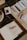 An arrangement of art materials including watercolors, paint tubes, and various paintbrushes is displayed on a wooden table. A book titled 'The History Book' lies open, alongside a spiral-bound sketchbook labeled 'ART'. A woven placemat and a striped mug are partially visible.
